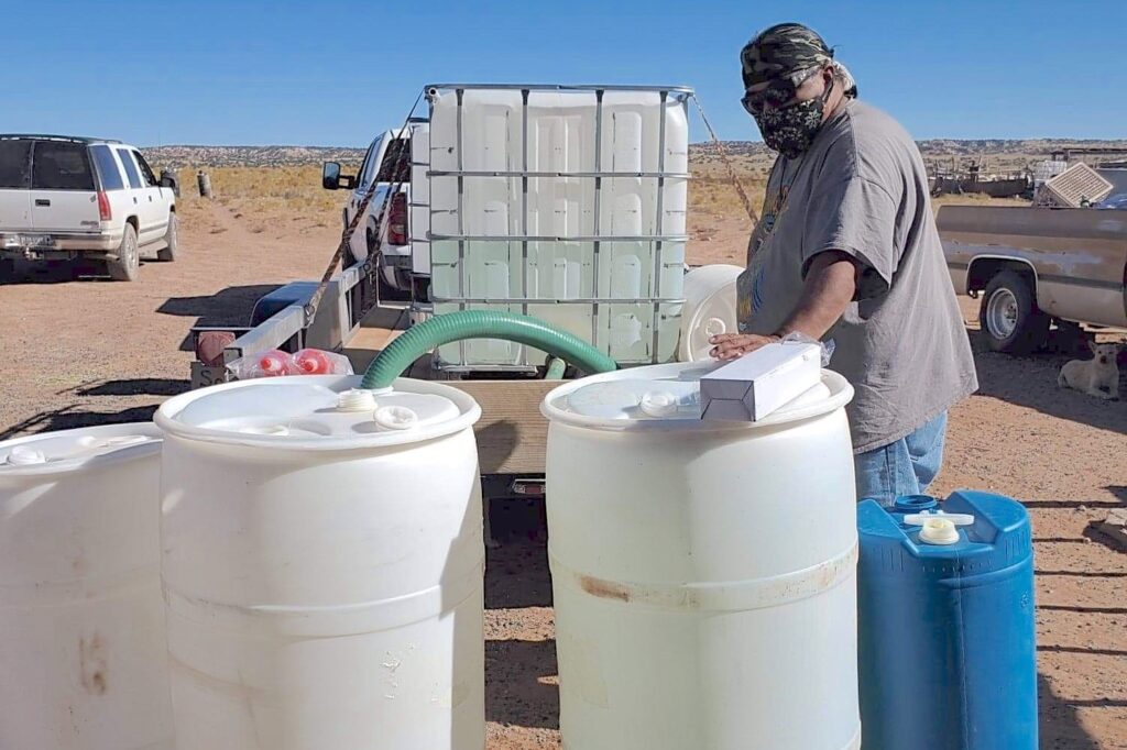 Photo of a person filling large plastic barrels with drinking water