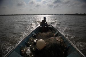 Person in shadow on a long, narrow boat on a large body of water